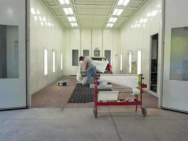 Technician masking a vehicle inside the downdraft paint booth at Jim Winter Auto Body